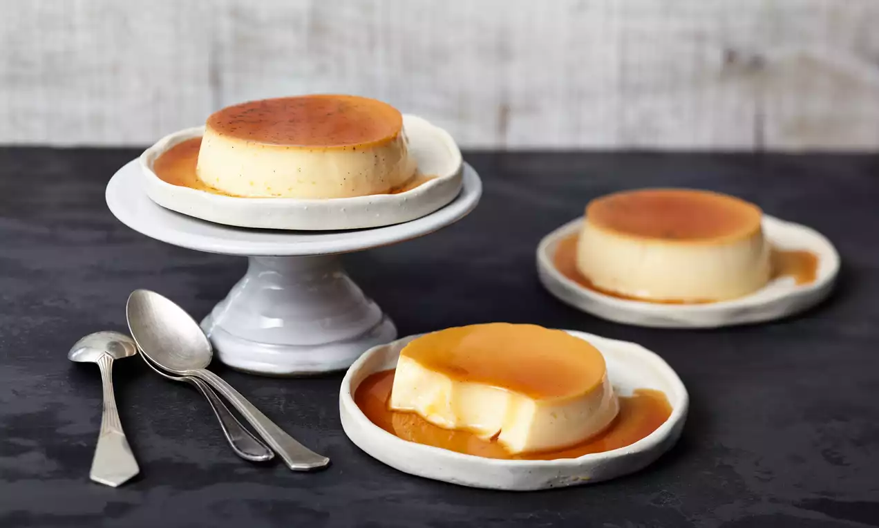 Crème Caramel mit glänzender goldbrauner Karamellsoße auf cremigem hellgelben Pudding, garniert mit einer Vanilleschote auf weißem Teller