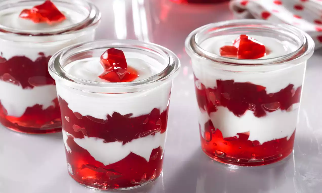 Copos de vidro com camadas alternadas de iogurte branco cremoso e gelatina vermelha brilhante, decorados com pedaços de gelatina