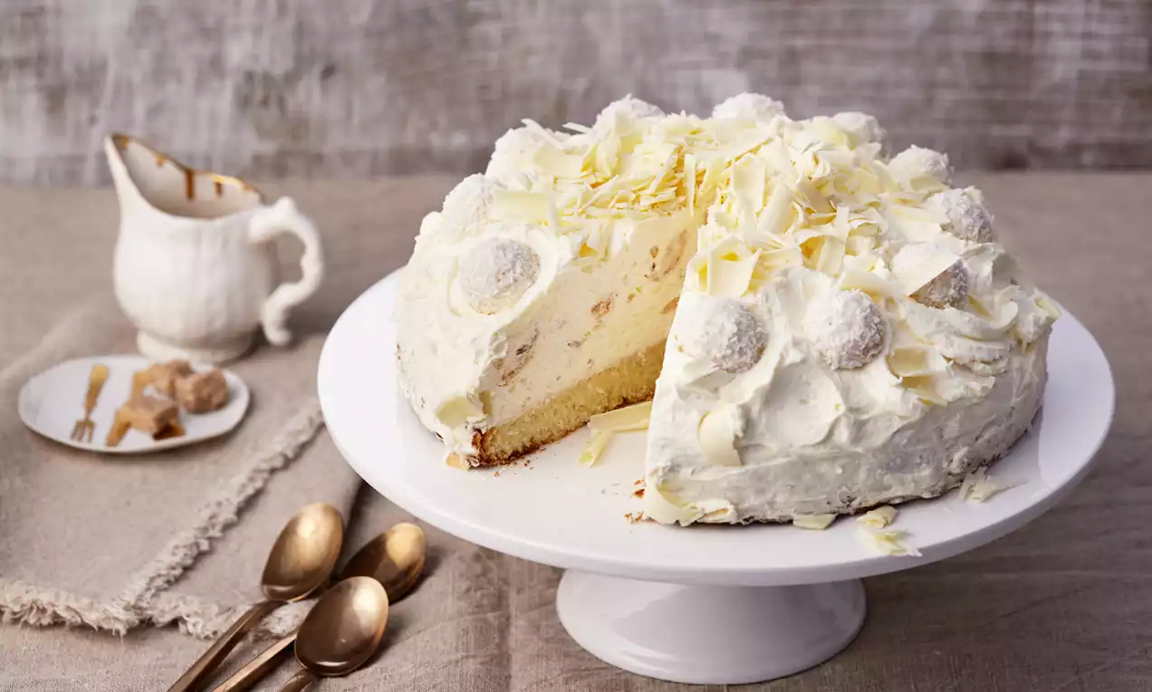 Raffaello®-Torte mit weißer Cremeschicht, feinem Biskuitboden, Kokoskugeln und weißen Schokoraspeln auf einer weißen Tortenplatte