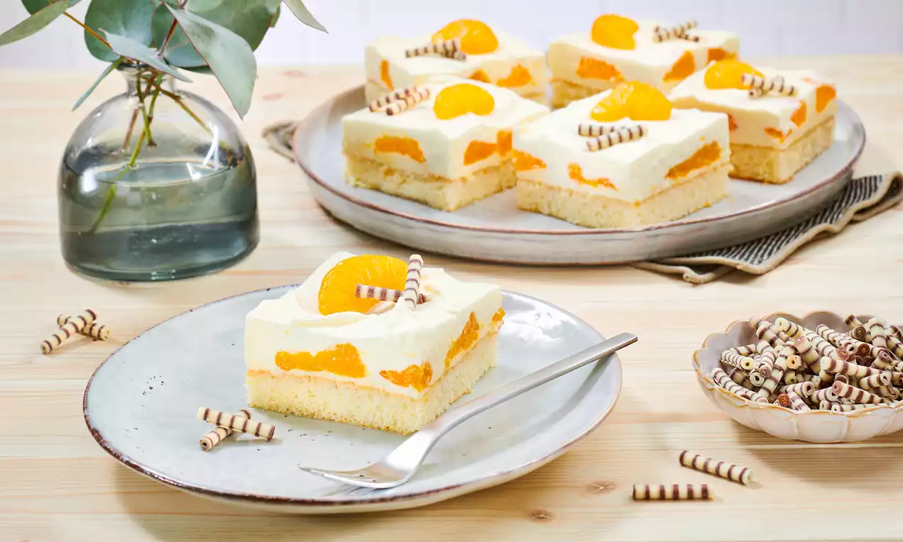 Quadratische Mandarinen-Schmand-Schnitten mit hellem Boden, weißer Creme, fruchtigen Mandarinenstücken und dekorativen Schokoröllchen