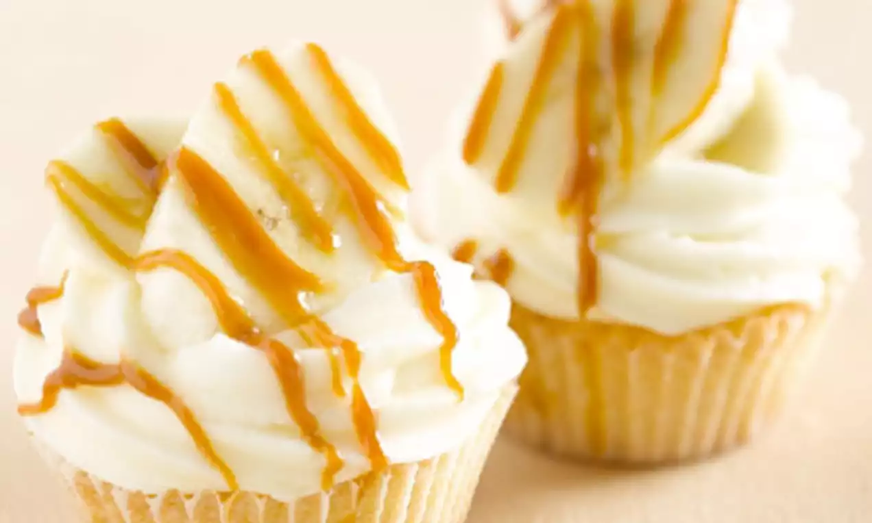 Cupcakes dorés surmontés de crème blanche onctueuse, morceaux de banane et filet de caramel ambré sur un fond beige chaleureux