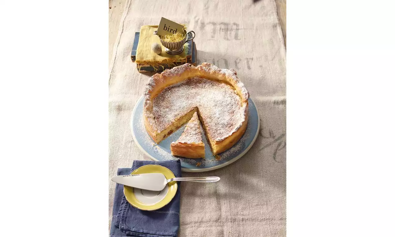 Tarte au riz dorée à la croûte légèrement gonflée, saupoudrée de sucre blanc sur une assiette bleue avec une part découpée et servie.