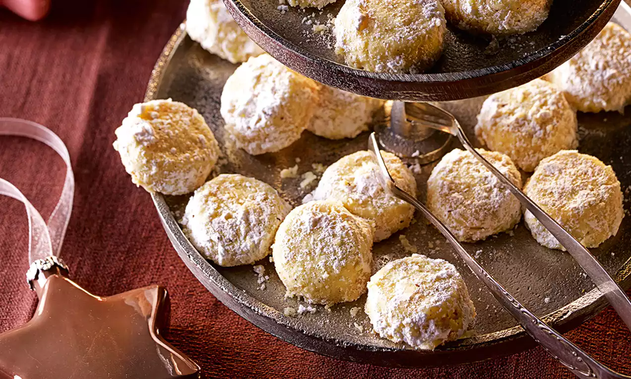Petits biscuits poudrés de sucre glace, ronds et dorés, disposés en étages sur un plat en métal sombre avec une étoile décorative