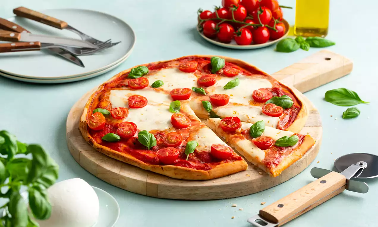 Ronde pizza met een goudbruine krokante korst, rode tomatensaus, gesmolten witte kaas, felrode cherrytomaatjes en groene basilicum op een houten plank