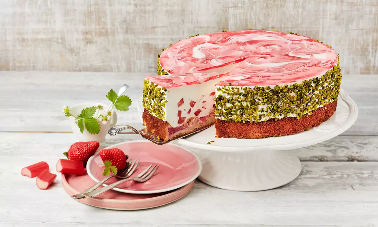 Rhabarber-Erdbeer-Torte mit rosa-weißem Marmormuster, fruchtiger Füllung und grünem Pistazienrand auf weißer Tortenplatte