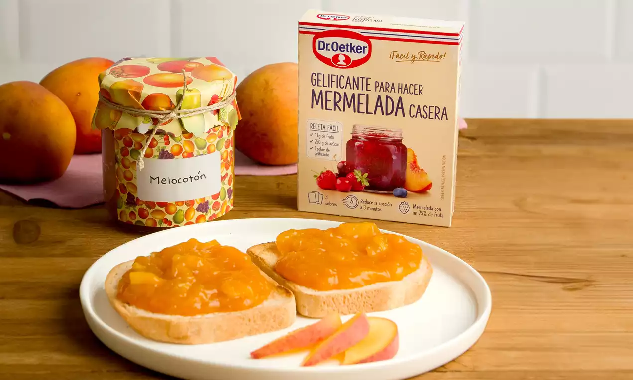 Tostadas doradas cubiertas con mermelada de melocotón de color anaranjado brillante, acompañadas de rodajas finas y melocotones al fondo