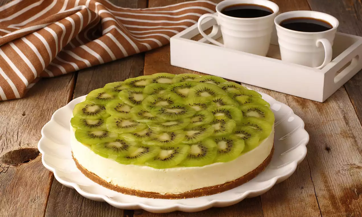 Altın rengi bisküvi tabanlı, kremsi beyaz dolgulu ve düzenli dilimlenmiş canlı yeşil kiviyle süslenmiş cheesecake