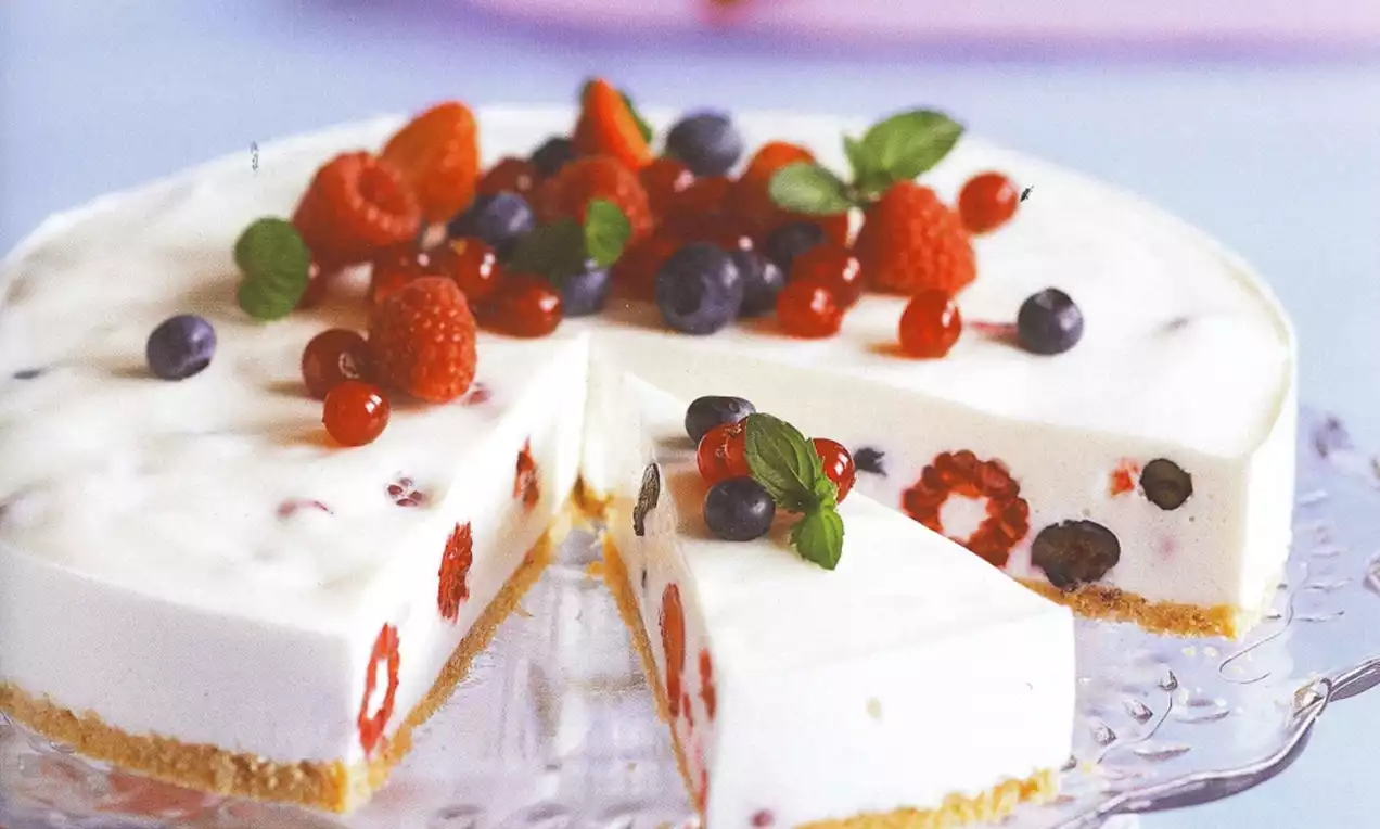 Bavarois blanc crémeux sur base biscuitée dorée garni de framboises, myrtilles et feuilles de menthe disposés en couronne sur le dessus
