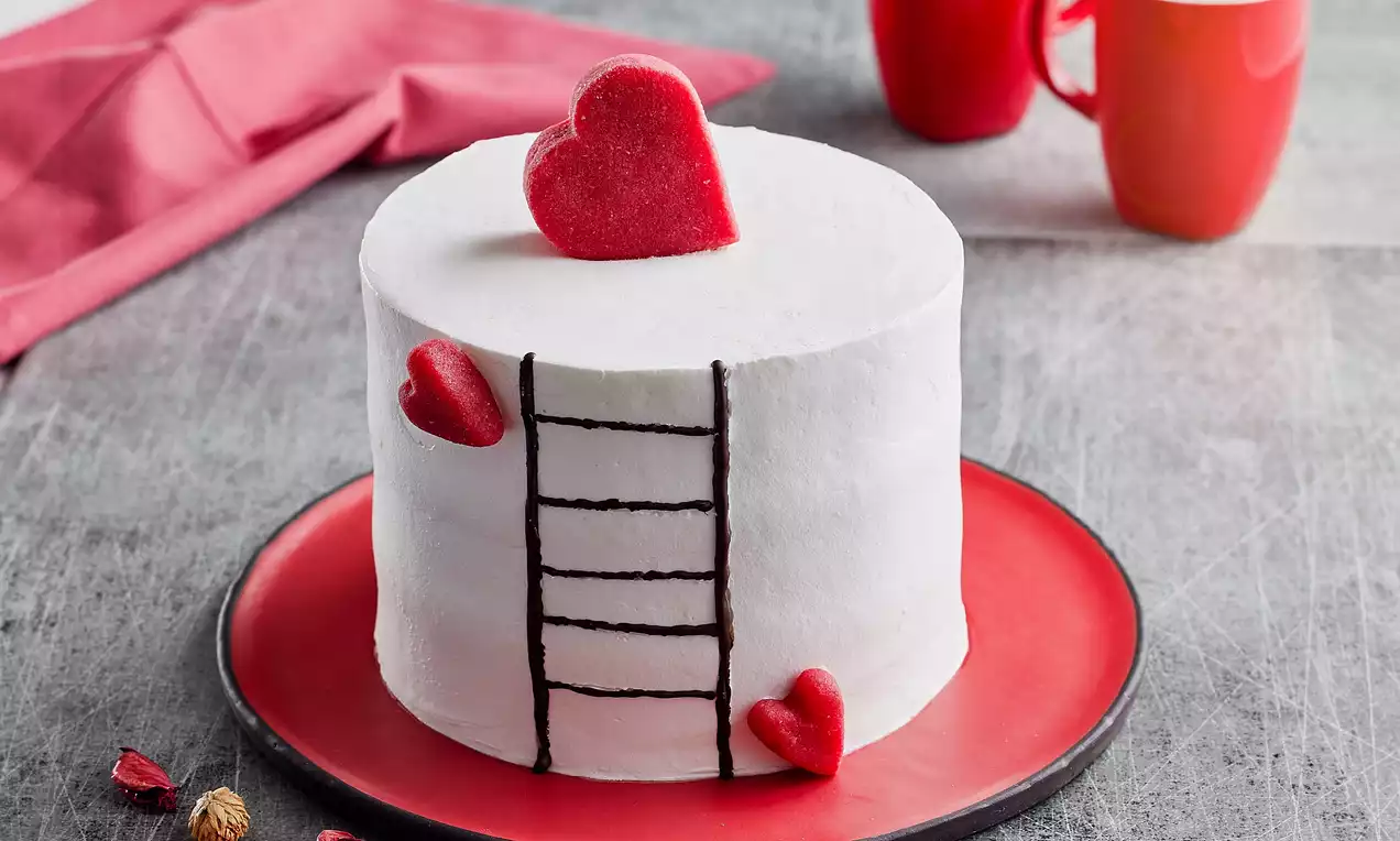 Beyaz krema kaplı, düz silindirik formda, kırmızı kalpler ve çikolatadan merdiven detayıyla kırmızı tabakta sunulan pasta