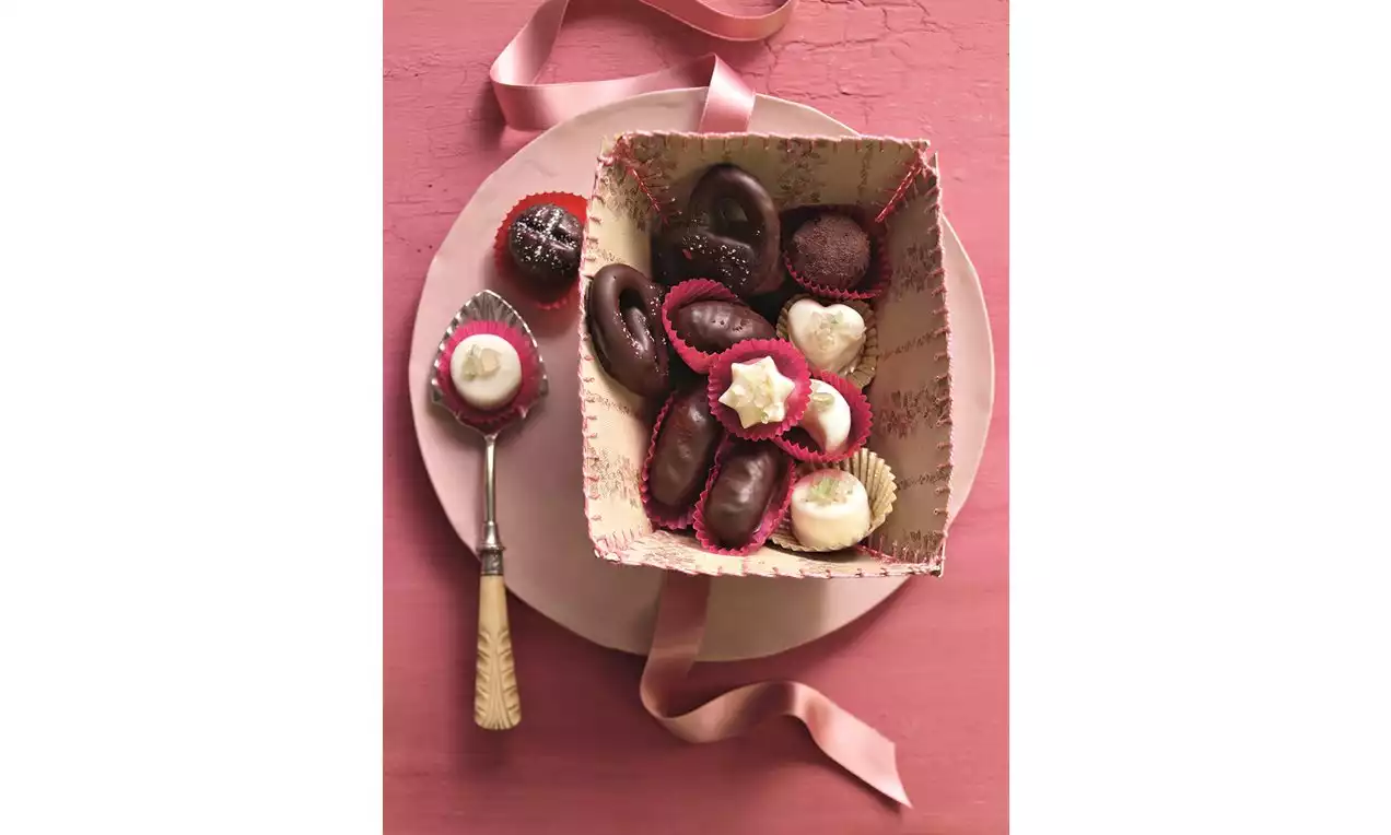 Marcipánové bonbony různých tvarů a barev v červených papírových košíčcích na růžovém talíři, vedle lžičky převázané růžovou stuhou