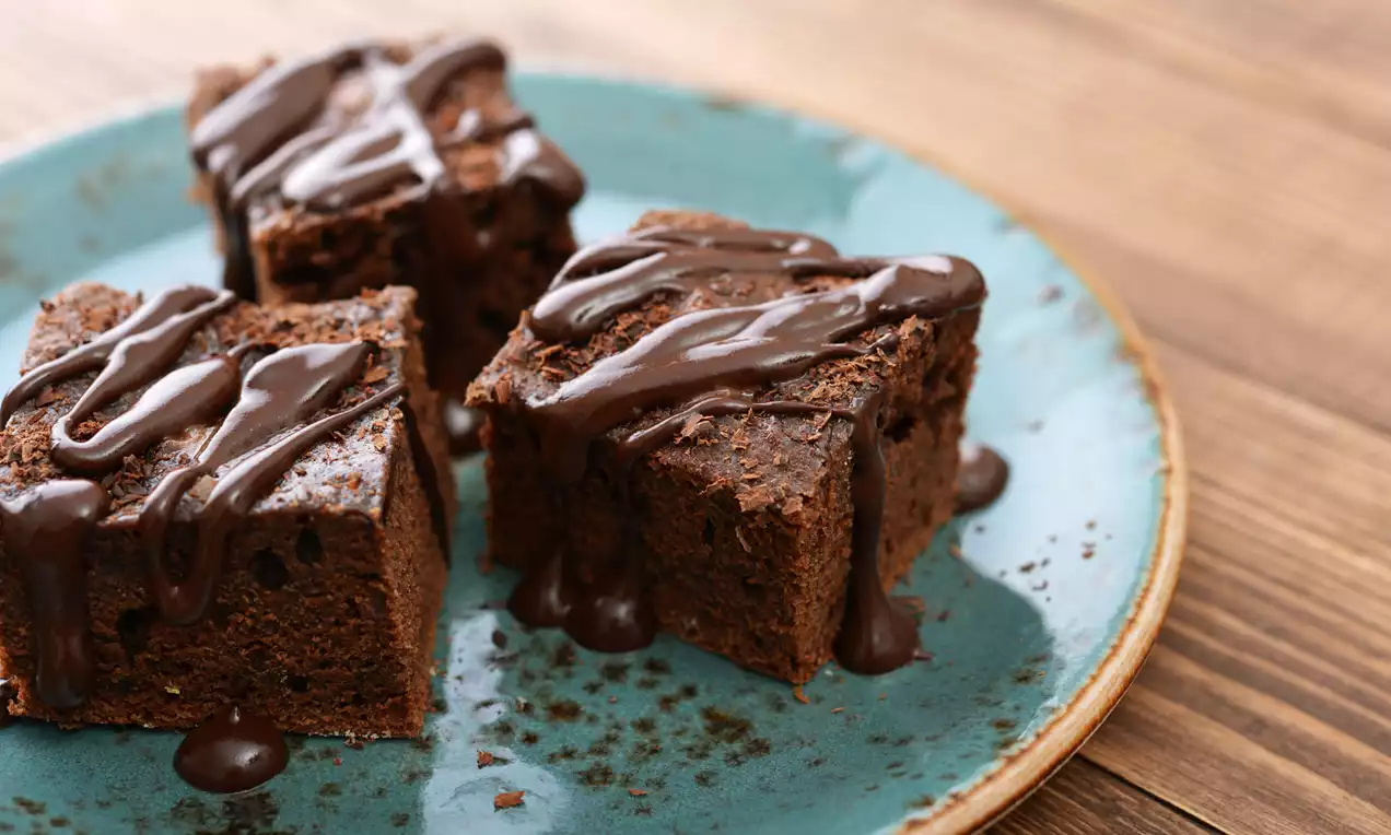 Brownies maison moelleux et denses, coupés en carrés, nappés de filets de chocolat fondant sur une assiette turquoise