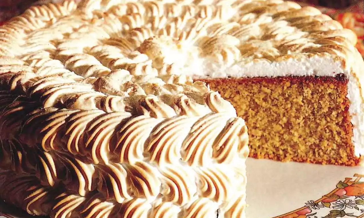 Ronde amandelslagroomtaart met goudbruin gebrande meringuepatronen en een groene spinaziebodem, geserveerd op een gebloemd bord