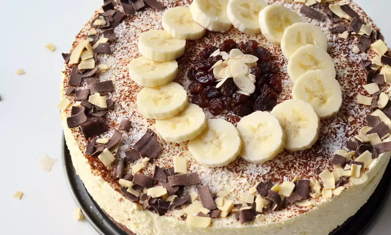 Kwarktaart met een romige gele vulling, decoratie van cacaopoeder, chocoladeschaafsel, bananenschijfjes en een midden van rozijntjes