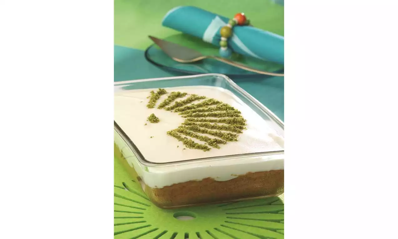 Kare cam kabın içinde tabanı kahverengi, üstü beyaz muhallebi kaplı ve üzeri ince yeşil toz fıstık desenli tatlı