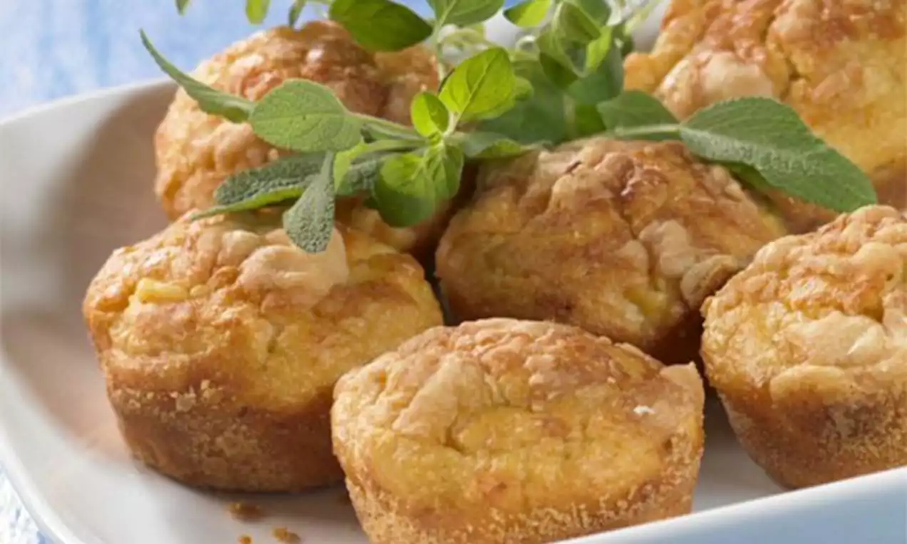 Muffins dorés au parmesan à la texture moelleuse et légèrement croustillante en surface, ornés de feuilles de basilic frais sur une assiette blanche