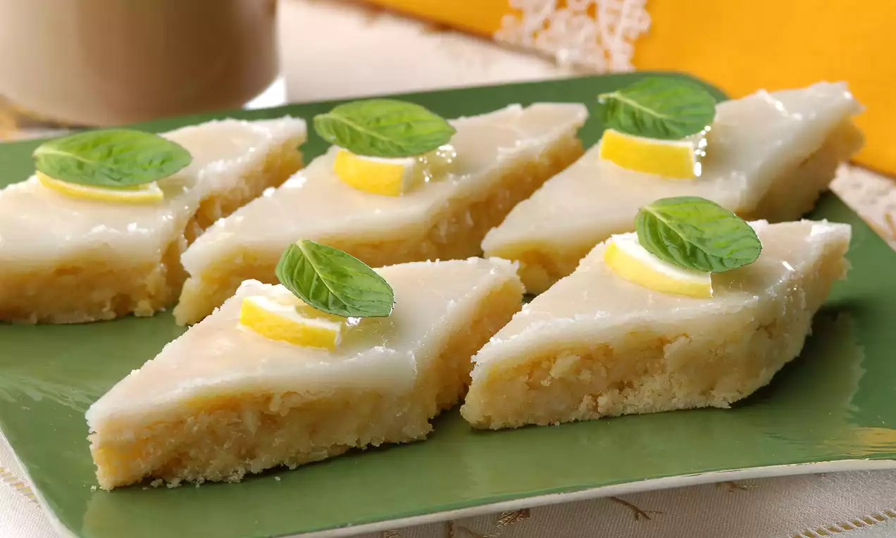 Yeşil tabakta sunulan, üçgen dilimlenmiş beyaz kaplamalı tatlı, limon dilimleri ve taze nane yaprakları ile süslenmiş