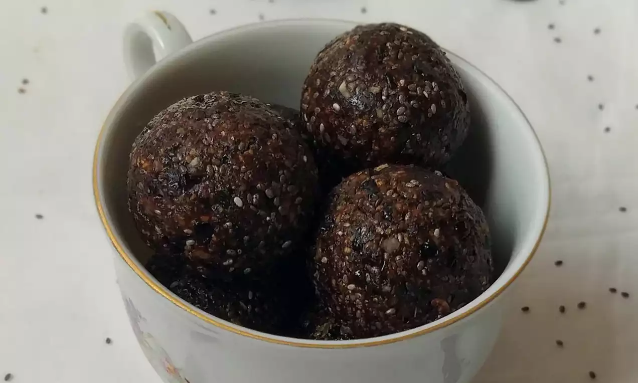 Tmavě hnědé švestkové kuličky s hrubou texturou a drobnými světlými zrníčky v bílé porcelánové misce na světlém podkladu