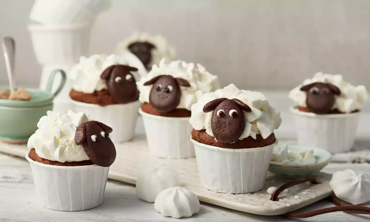 Čokoladni kolački v belih papirnatih modelčkih, z mehko kremo belega videza in čokoladnimi ovčjimi glavami z majhnimi sladkornimi očmi
