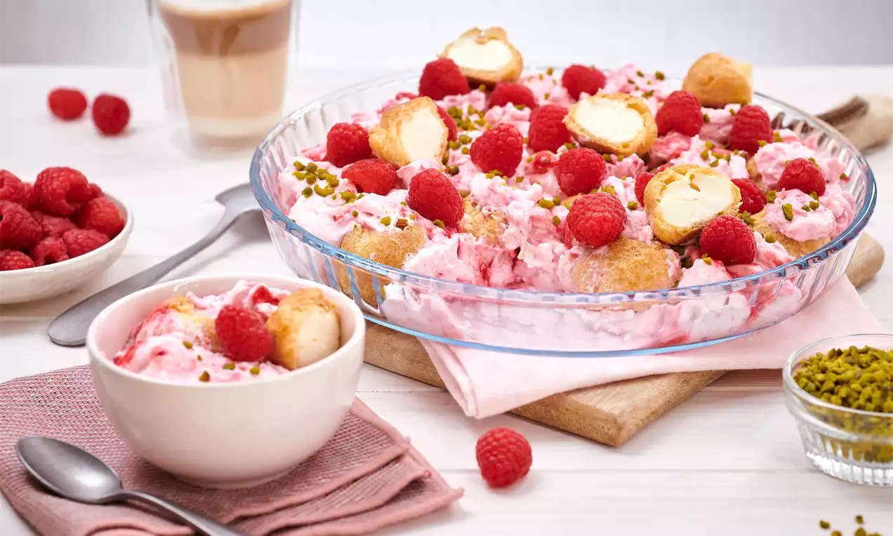 Windbeutel-Dessert mit zartrosa Mascarponecreme, frischen Himbeeren, Windbeutelstücken und gehackten Pistazien in einer Glaspieform