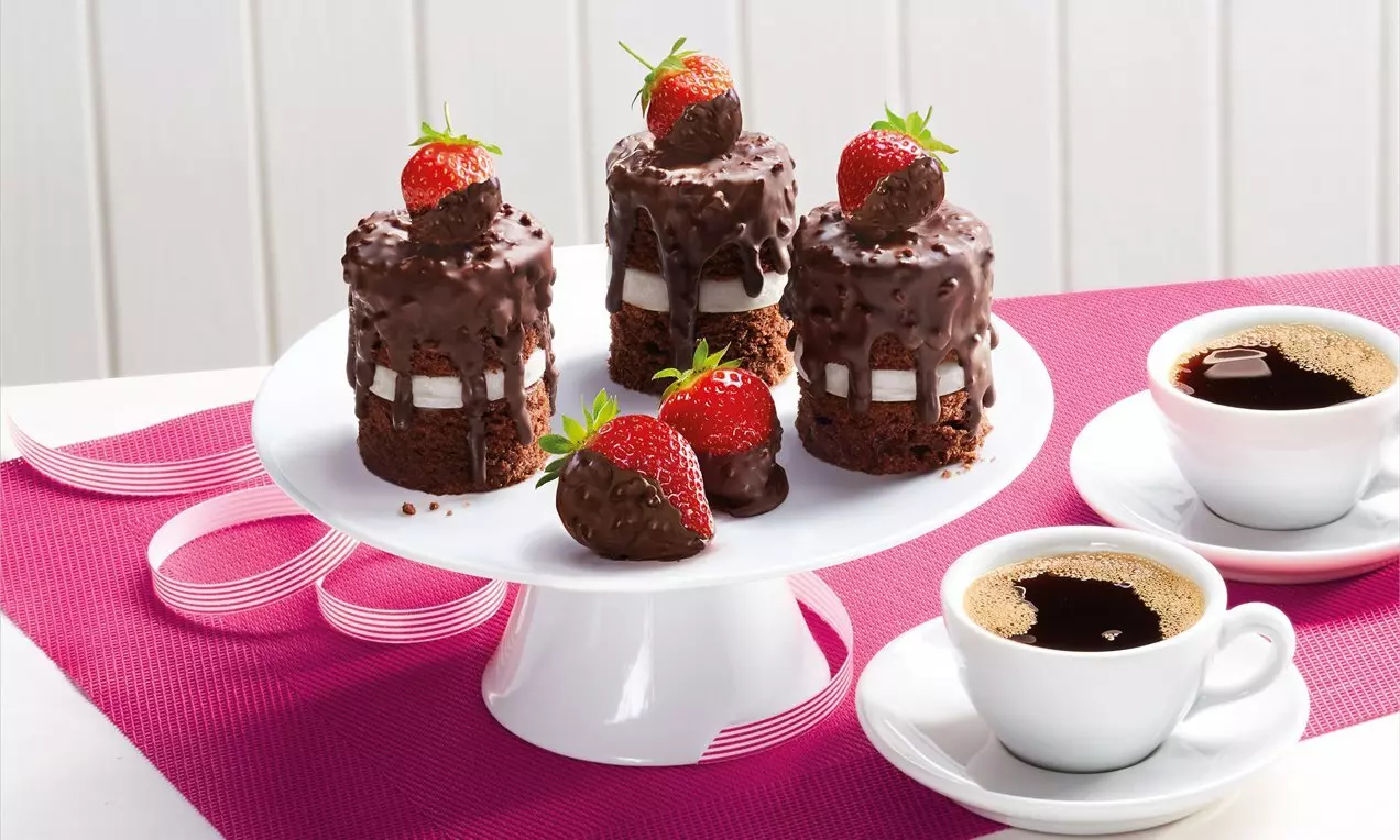 Мини шоколадови тартове с лъскава глазура, украсени със свежи ягоди, подредени върху бяла поставка върху ярък розов фон