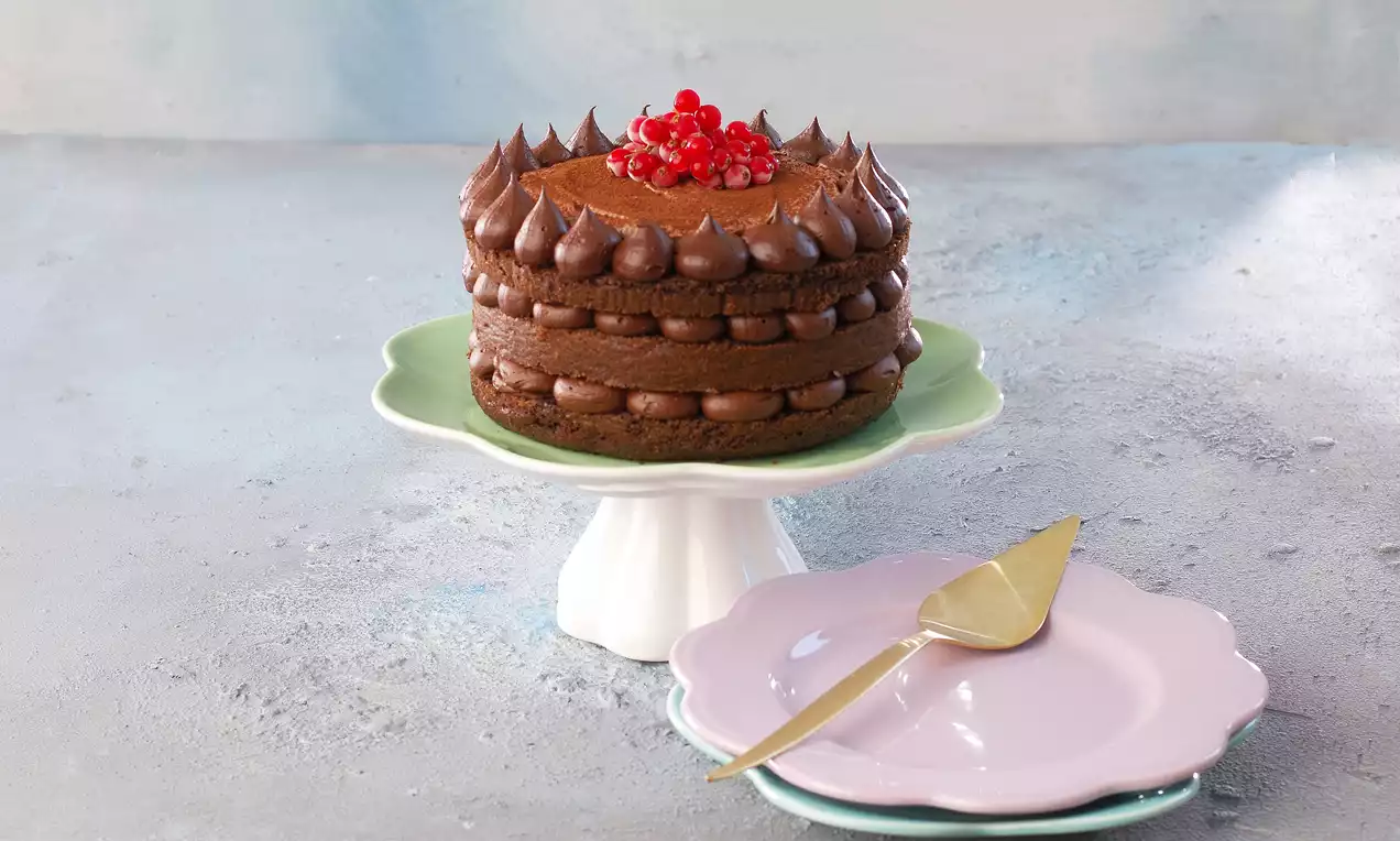 Üç katlı, krema dolgusuyla zenginleştirilmiş çikolatalı pasta, üzeri kırmızı meyve taneleriyle süslenmiş ve pastel renkli bir ayakta sunulmuş