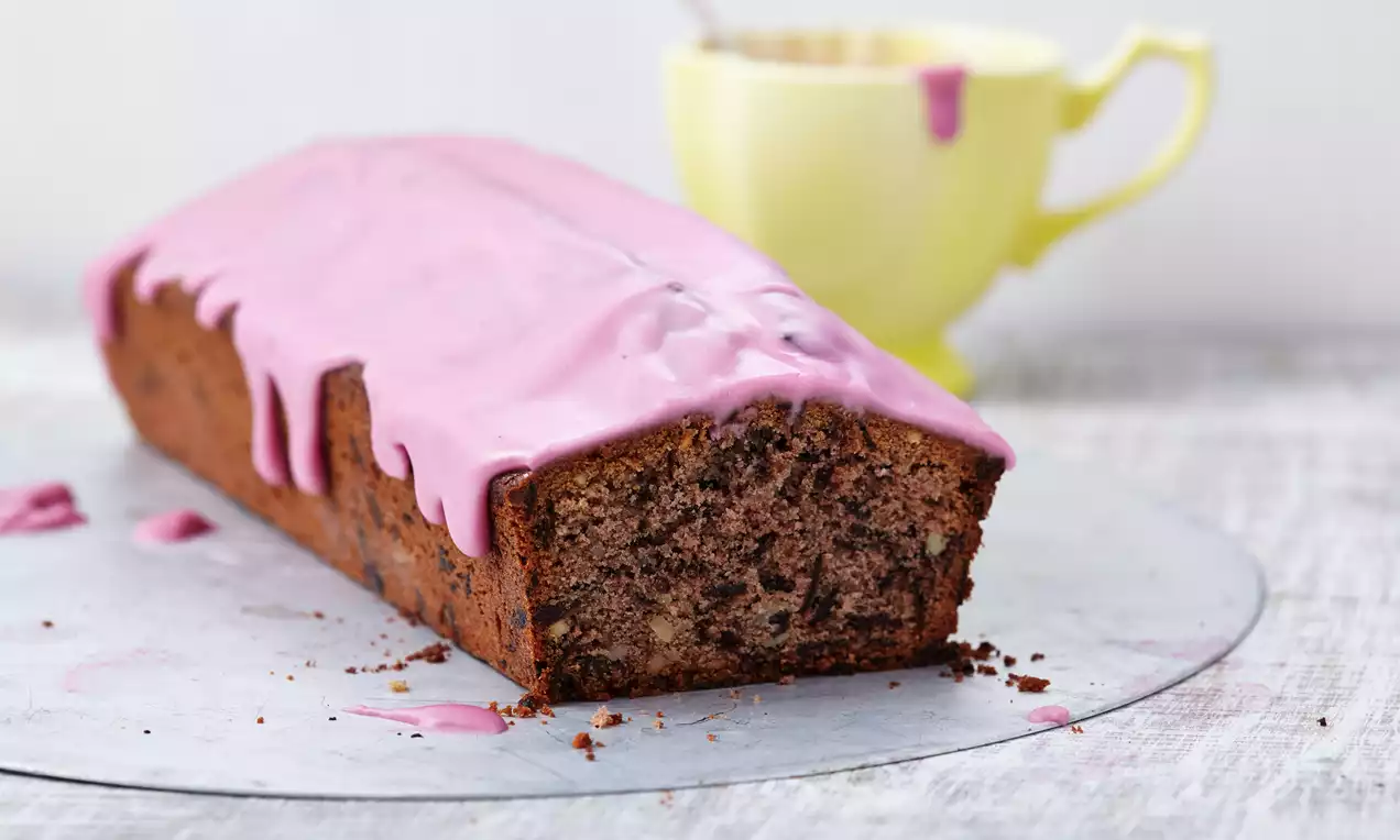 Rotwein-Kuchen mit leicht glasiertem rosa Zuckerguss auf silbernem Untergrund, daneben eine gelbe Tasse mit pinken Glasurresten