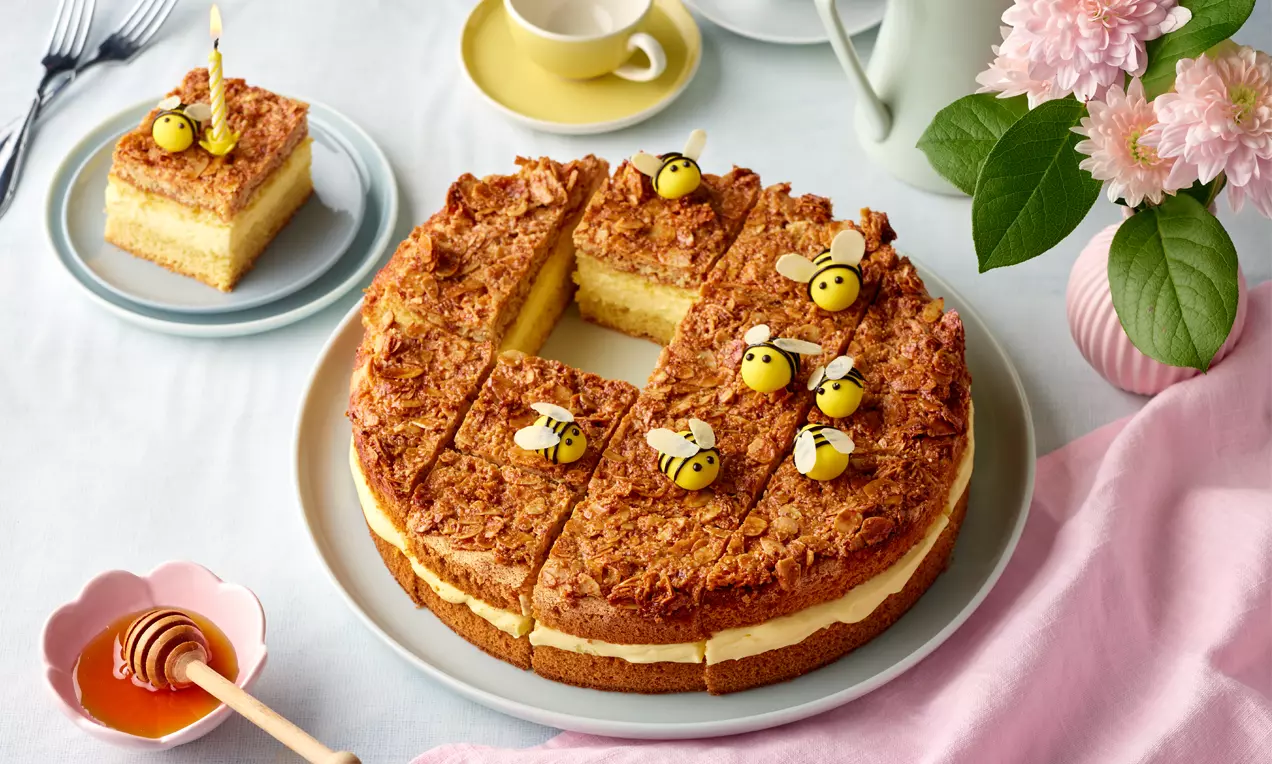 Runder Bienenstich mit goldbrauner Mandelschicht, heller Cremefüllung und Zuckerdekoren in Bienenform auf weißer Kuchenplatte