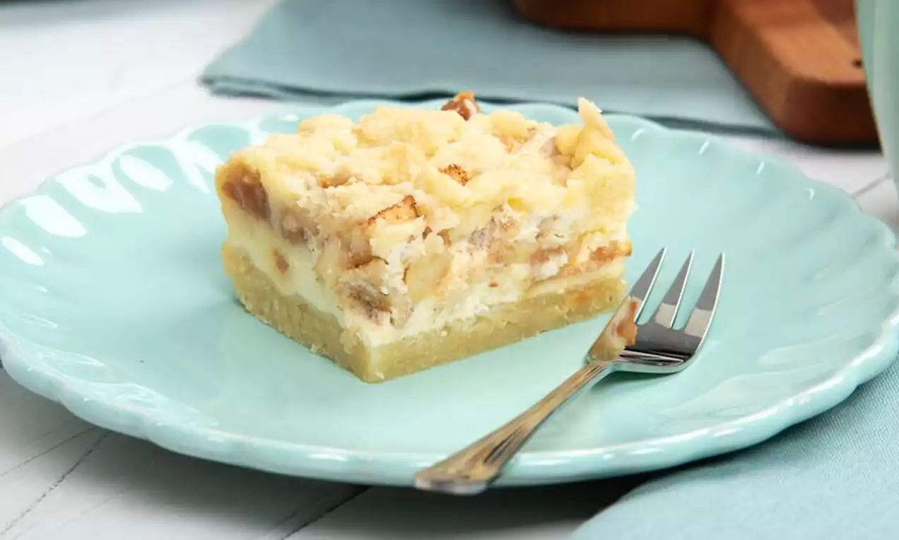 Ein Stück cremiger Caramel Apple Cheesecake mit hellen Streuseln und Apfelstücken auf einem zartblauen Teller mit silberner Gabel