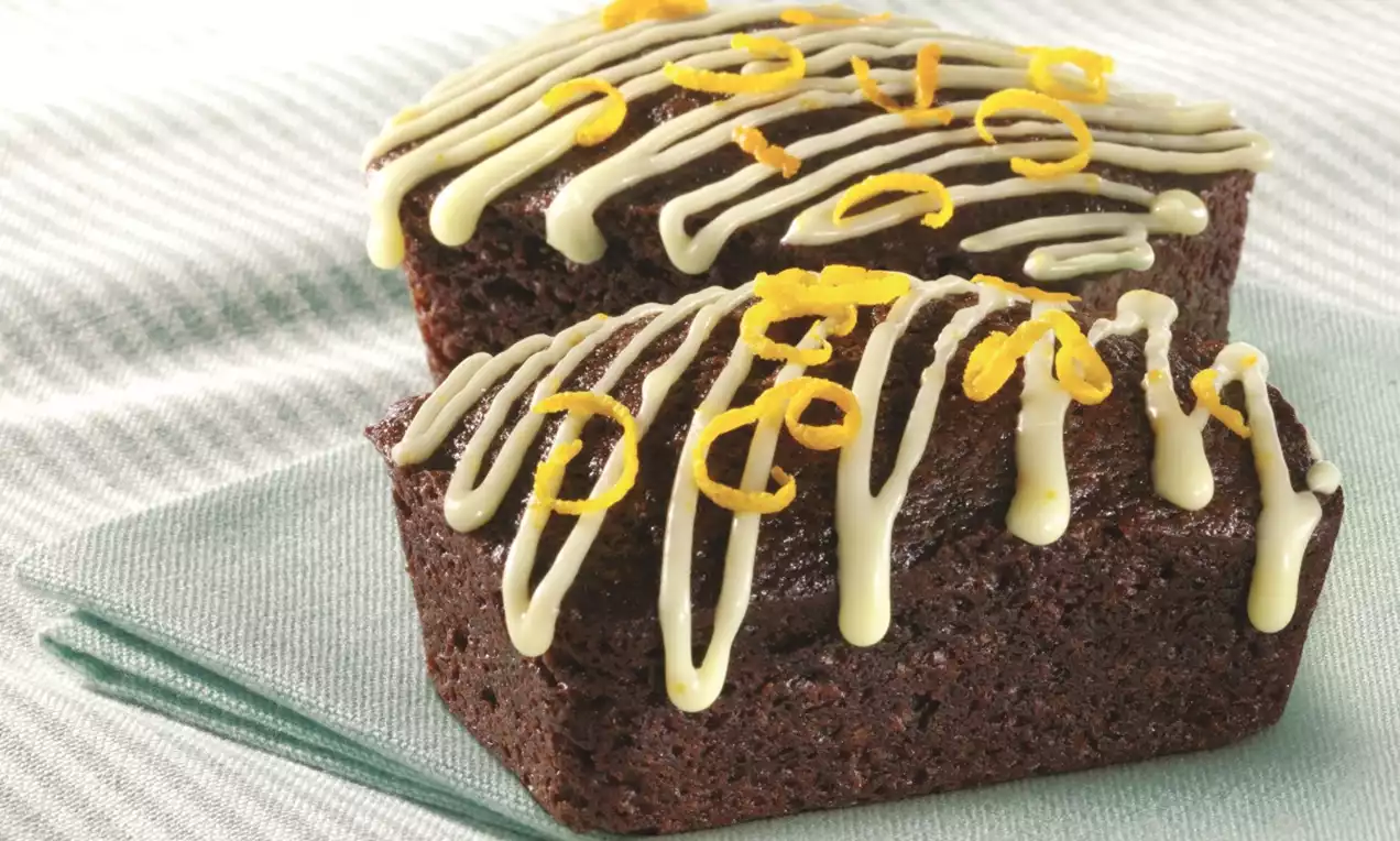 Mini ginger and orange loaf cakes with a rich brown crumb, drizzled with pale icing and scattered with bright orange zest
