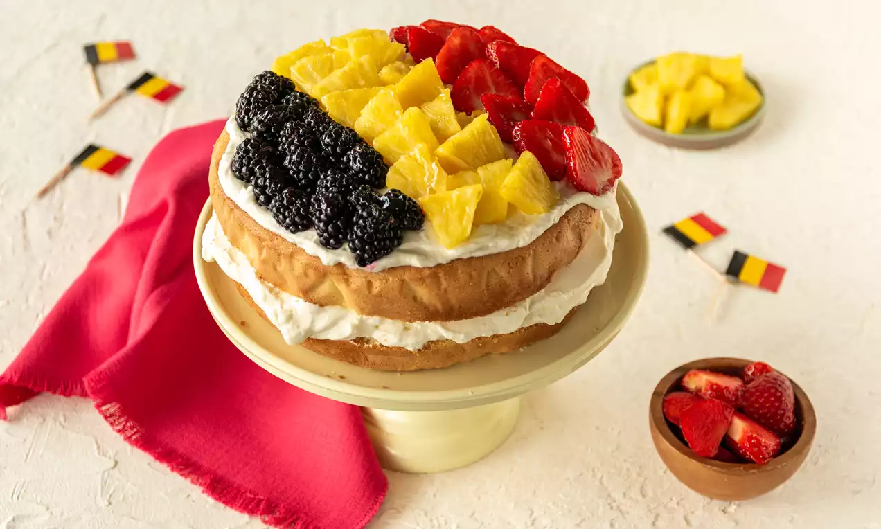 Tarte ronde légère garnie de crème blanche, décorée de mûres noires, cubes d'ananas jaunes et fraises rouges disposés en bandes