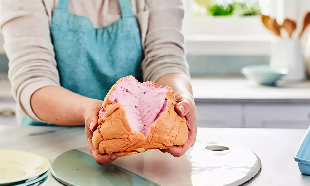 Fluffy cloud bread with a golden-brown crust and light pink airy center held in hands over a kitchen counter with plates nearby