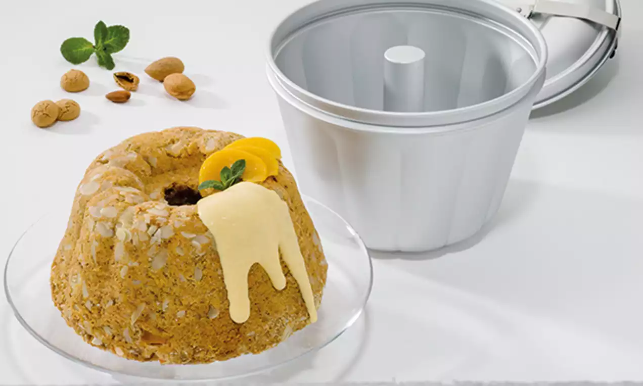 Goldbraune Puddingform mit Amarettini-Stückchen auf Glasplatte, dekoriert mit hellgelber Sauce, Pfirsichspalte und Minzblatt