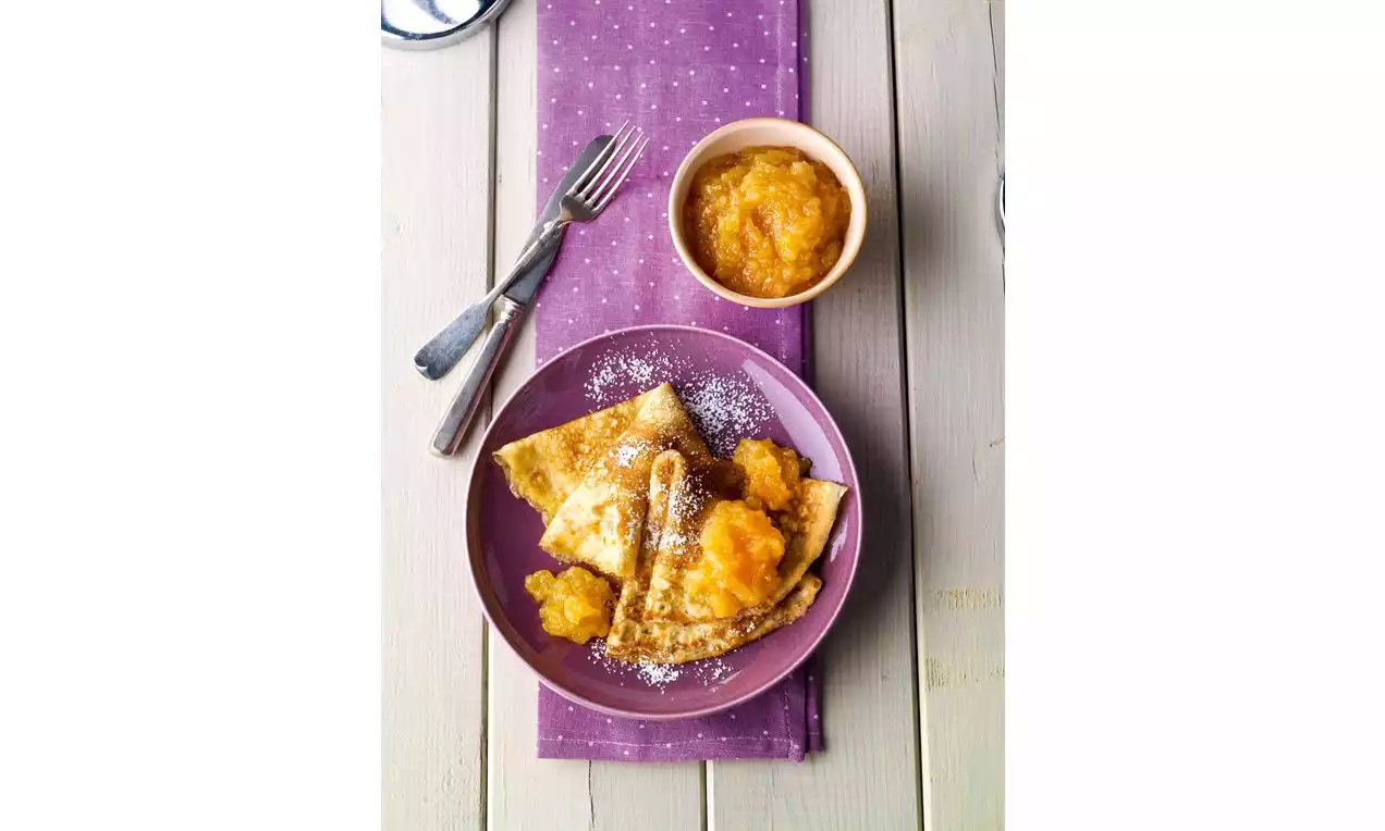 Crêpes dorées pliées en triangles, garnies de confiture de coing ambrée et saupoudrées de sucre glace dans une assiette violette