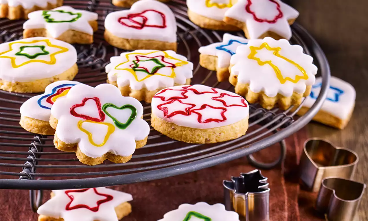 Biscuits en pâte dorée recouverts de glaçage blanc décorés de motifs colorés en forme de cœurs, étoiles et comètes sur une grille ronde