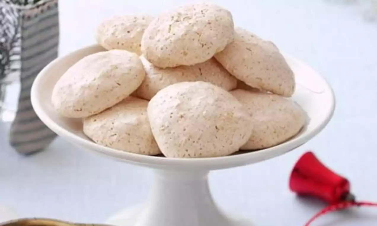 Lysebrune kokosmakroner med lett sprø overflate og ujevn tekstur ligger i en haug midt på et hvitt kakefat