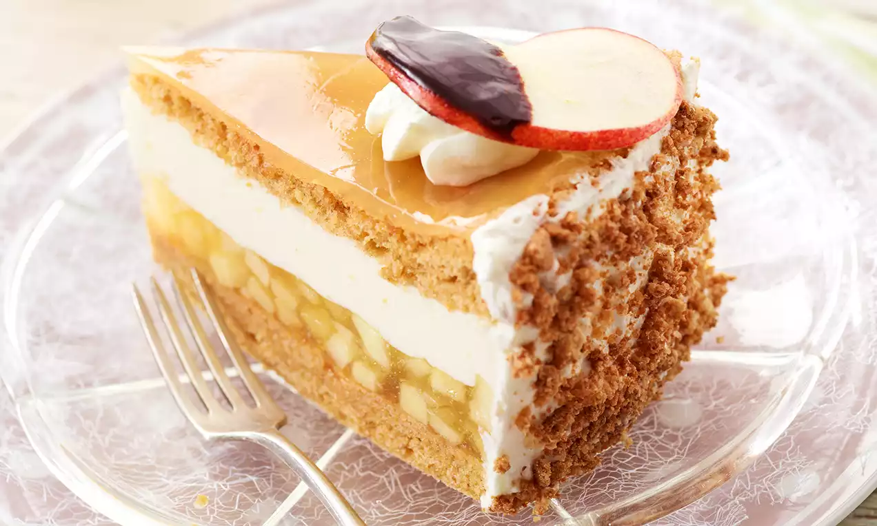 Part de gâteau aux pommes avec couches de crème blanche, éclats dorés de fruits, bord croustillant et tranche de pomme nappée de chocolat