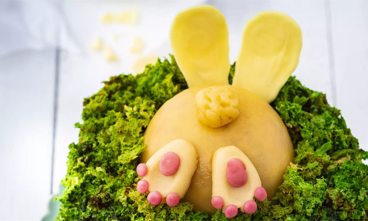 Светлокафяво заешко тяло от гладък марципан с кремообразна текстура, оформено сред зелена основа, с розови лапички и ушички от жълт шоколад