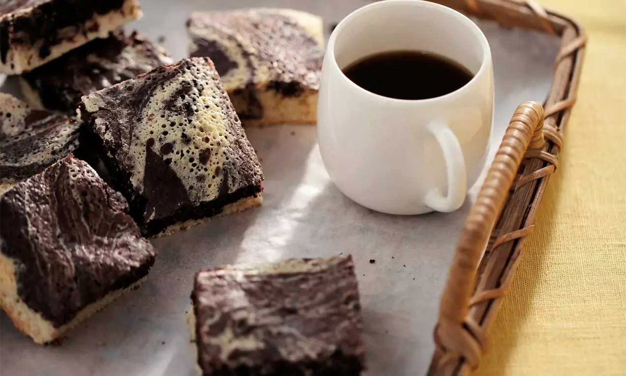 Nelielos gabaliņos griezts marmora kūkas deserts ar kontrastējošām tumšajām šokolādes un gaišajām vaniļas virpuļveida tekstūrām uz paplātes