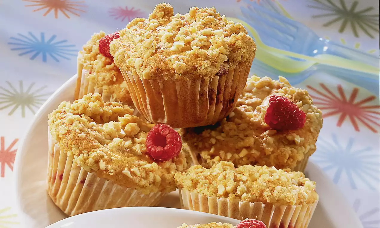 Muffin dorati con streusel croccanti, punteggiati di lamponi rosso vivo, disposti su un piatto bianco con un vivace sfondo colorato