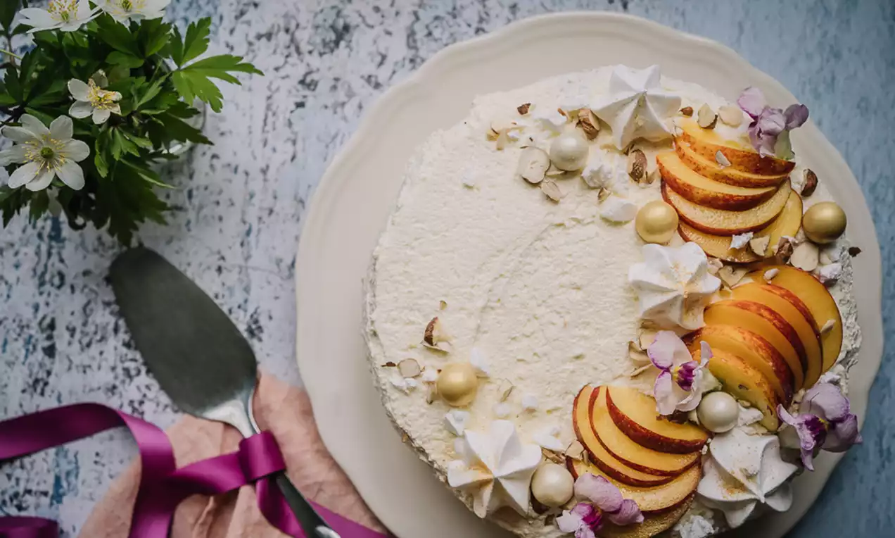 Nektarinmoussetårta med krämigt vit yta, dekorerad med nektarinskivor, små maränger, blommor och chokladkulor på ljus tallrik