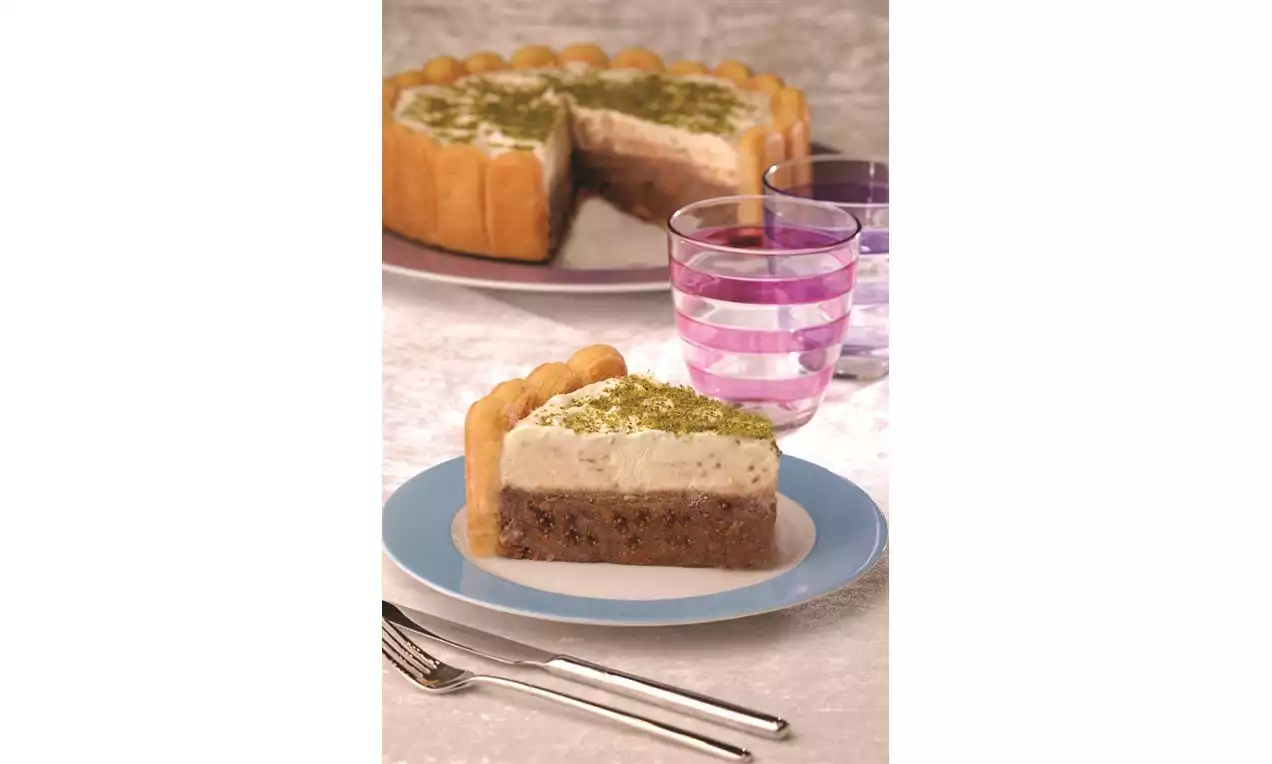 Yuvarlak tabakta servis edilen dilim, kremalı üst katmanı ve fıstık tozu ile süslenmiş, kenarlarında bisküvi sıralı, iki katlı pandispanya