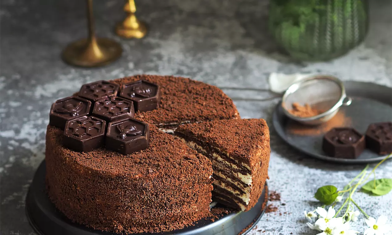 Кръгла торта с медени слоеве и крем между тях, покрита с кафяв стръготинен слой и декорирана с шоколадови медени пити върху метална чиния