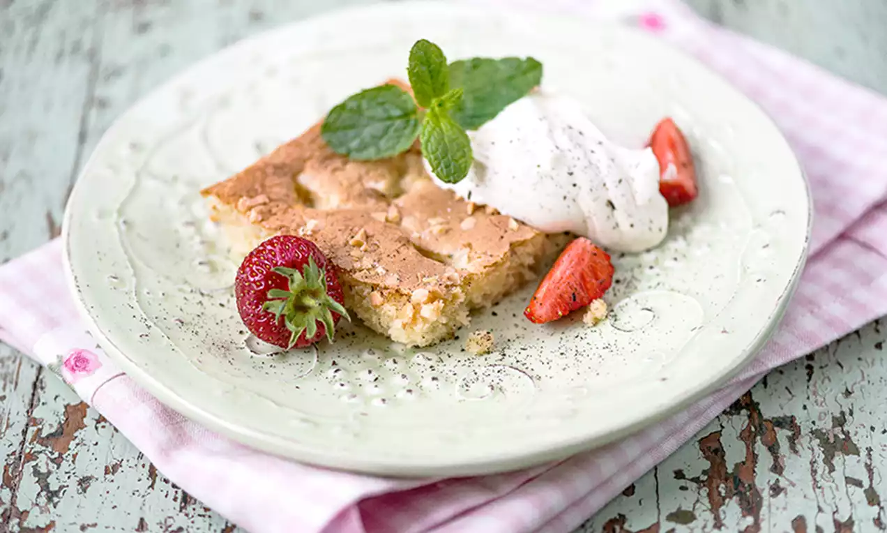 Vaaleanruskea, rapeapintainen raparperipiiraan siivu pastellisella lautasella, mascarponevaahtoa, mansikkapaloja ja mintunlehtiä somisteena