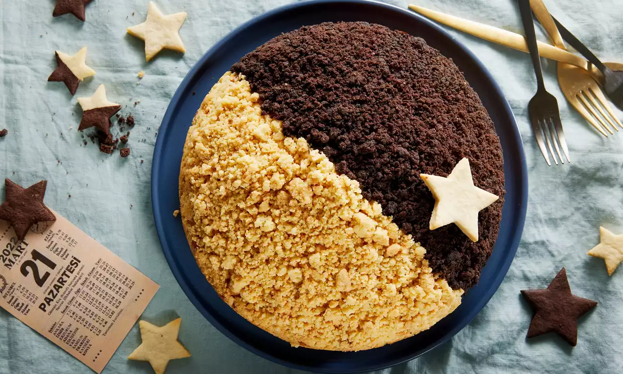 İki yarısı sarı ve kahverengi kırıntılarla kaplanmış, yıldız kurabiyelerle süslenmiş yuvarlak kek koyu mavi bir tabakta