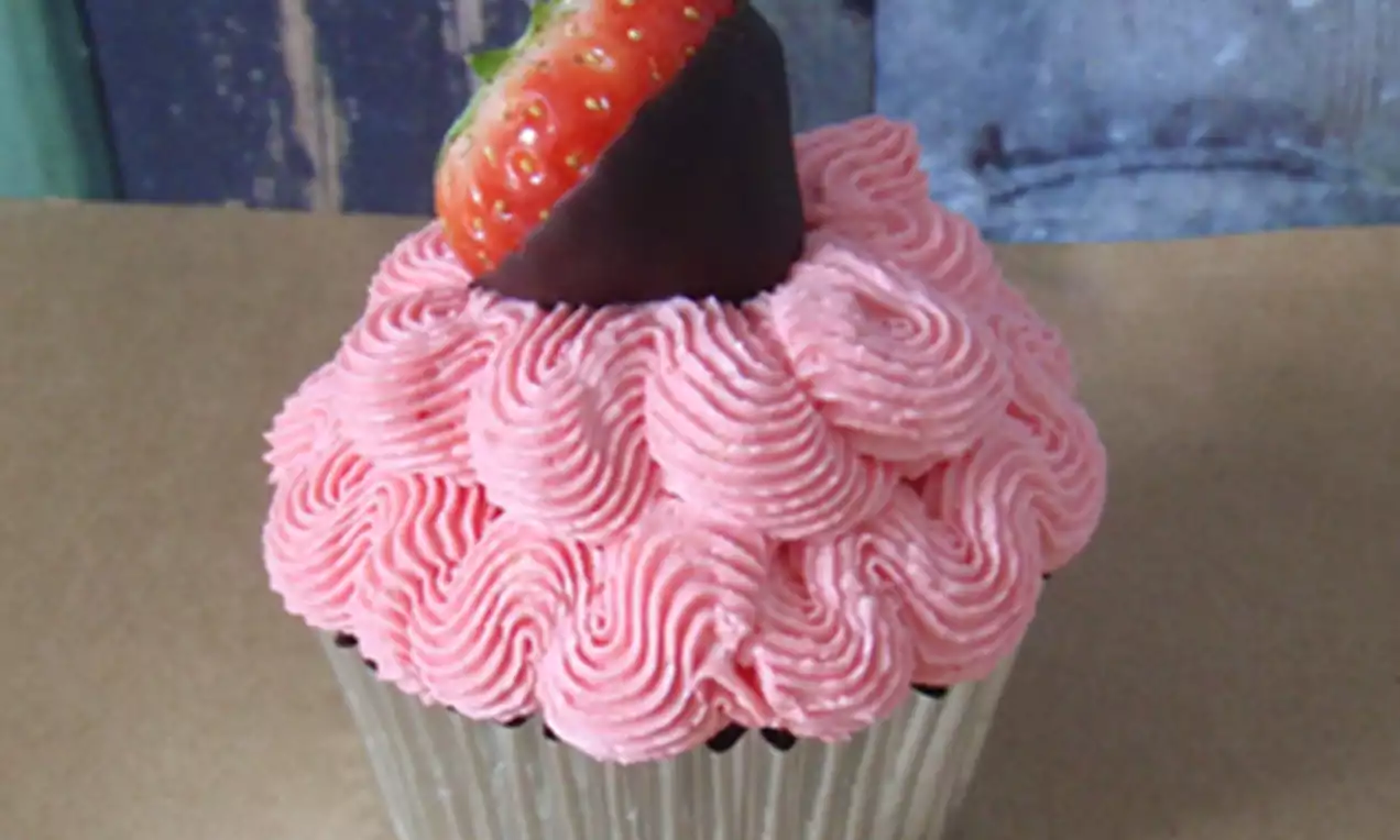 Cupcake met roze, gegolfde slagroom en een aardbei met glanzende donkere chocoladedip, geplaatst op een zilverkleurig bakvormpje