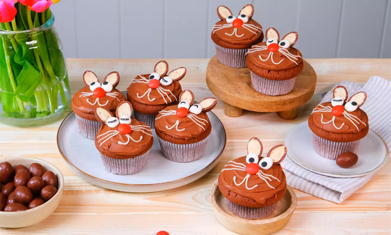 Chocoladecupcakes met bruine frosting en decoratie van witte en rode suiker, amandeloren en getekende snorharen op houten en witte borden