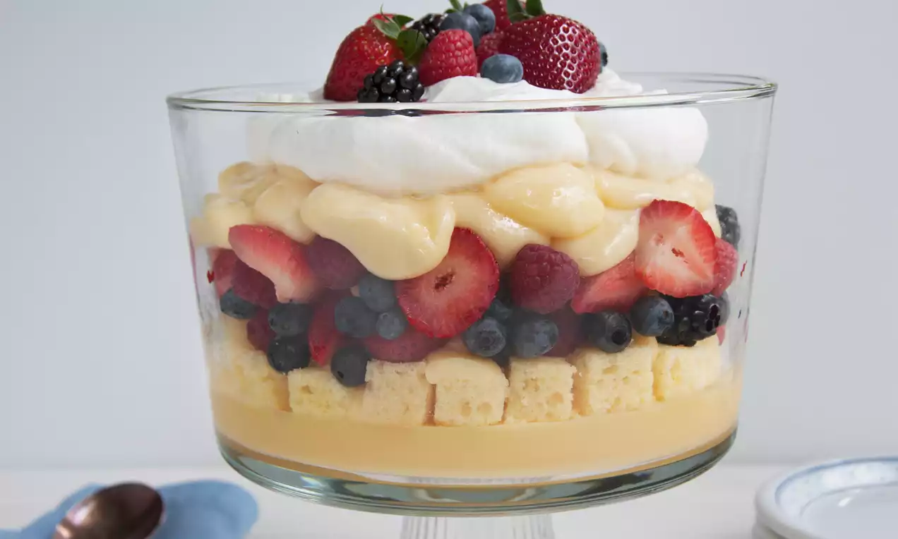 Trifle vanille aux couches de crème jaune pâle, fruits rouges frais et génoise moelleuse, couronné de chantilly blanche dans un verre élégant