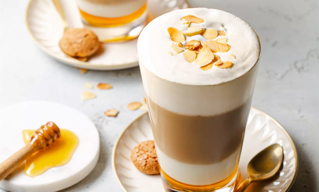 Picture - Layered almond coffee with frothy white cream, topped with golden almond slices, served in glass cups on white plates with amaretti