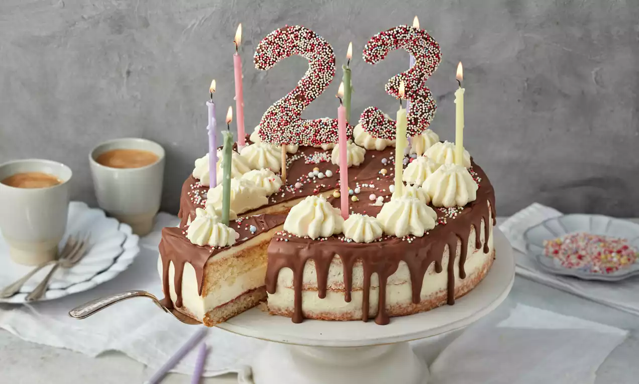 Geburtstagstorte mit Schokoladenglasur und Sahnetupfen, verziert mit bunten Kerzen und Zahlen aus Zuckerdekor auf einer weißen Platte