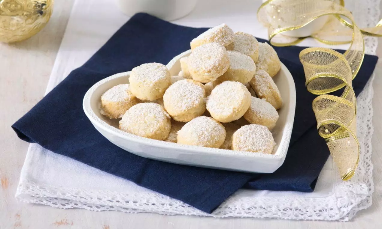 Vanilkové dukátky světlé barvy, kulatého tvaru, posypané moučkovým cukrem, uspořádané v bílé keramické misce na tmavě modré látce